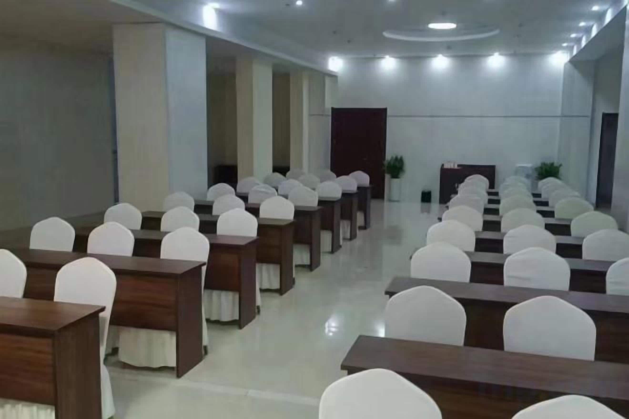 Un salón de conferencias con mesas y sillas dispuestas en filas, un atril y una planta grande.