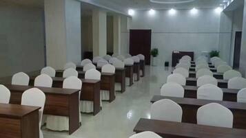 Un salón de conferencias con mesas y sillas dispuestas en filas, un atril y una planta grande.