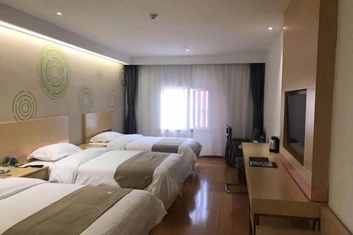 A hotel room with two beds, a desk, a TV, and a window with curtains.