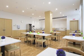 A dining area with multiple tables and chairs, a kitchen in the background, and a clock on the wall. - GreenTree Inn（Obeisar store, East Plaza, Xuzhou high speed railway station） (Xuzhou)