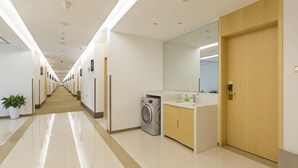 A hotel corridor with a long hallway, a washing machine, and a bathroom with a sink and mirror.