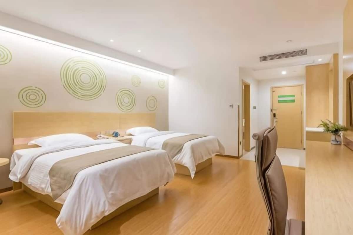A hotel room with two beds, a wooden headboard, a mirror, and a reception desk.