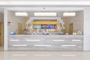 A hotel reception desk with a flat-screen TV, two receptionists, and a reception area with a marble floor and modern decor.