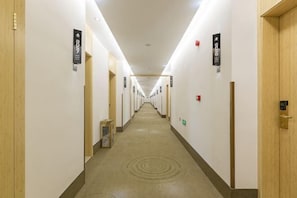 A long, narrow hotel corridor with doors on both sides, numbered signs, and a carpeted floor.