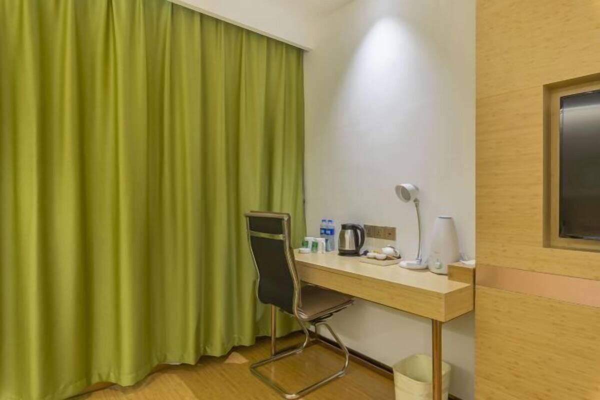 A hotel room with a wooden desk, a chair, a coffee maker, a lamp, and a trash bin.