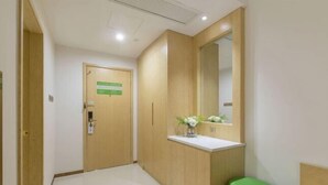 A hallway with a wooden door, a mirror, a green stool, and a white countertop.