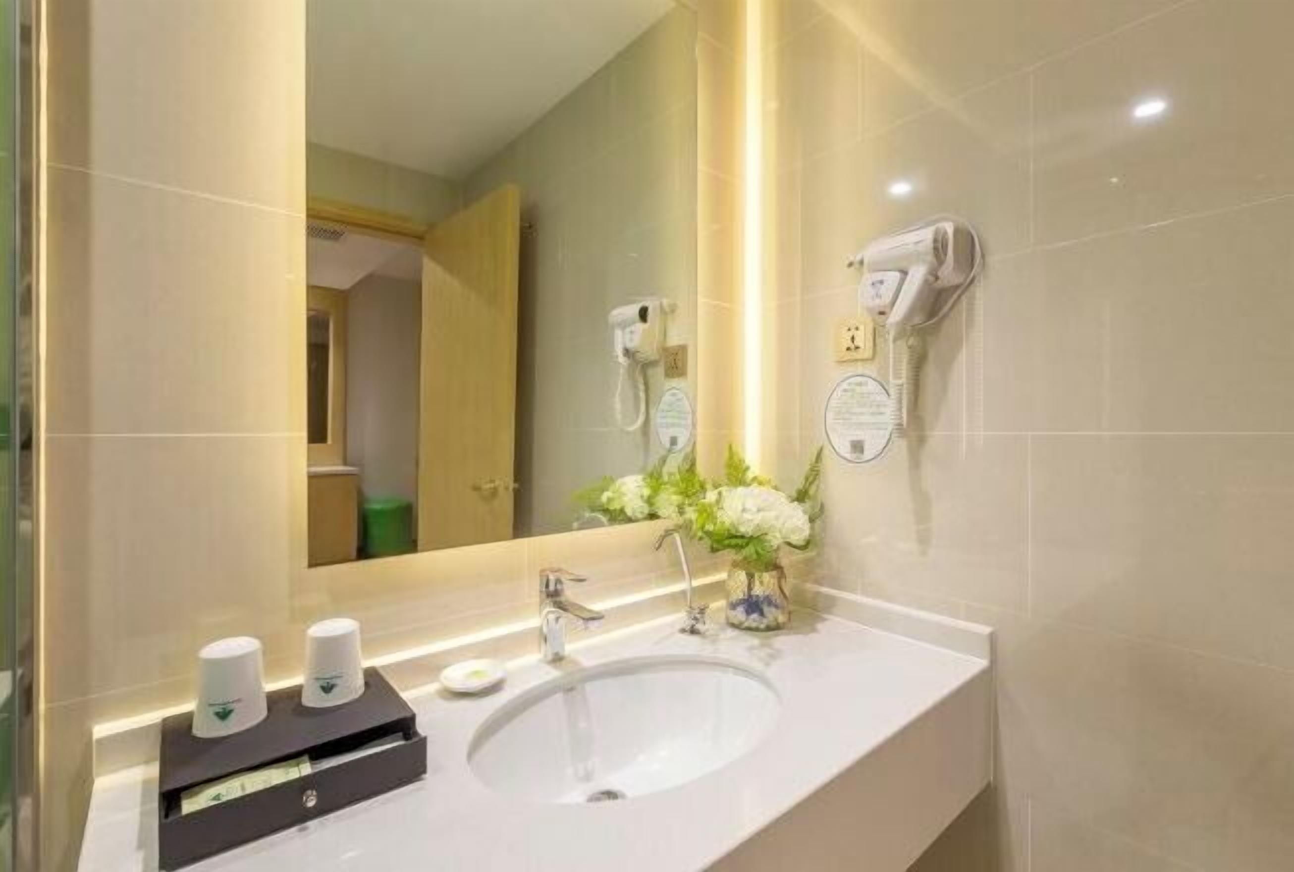 A modern bathroom with a large mirror, a sink, and a hairdryer mounted on the wall.