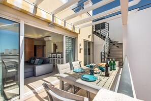 An open-plan living area with a dining table set for four, a sofa, and a staircase leading to an upper level. - Penthouse apartment in Cabanas Royal Beach with free WIFI & Pool. (Cabanas de Tavira)