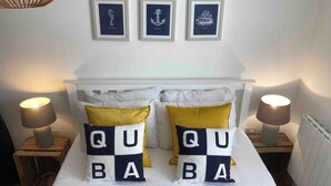 Una cama con cabecera blanca, dos lámparas de noche y almohadones decorativos que deletrean 'QUABA'.