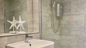 Un baño con un lavabo blanco, cabina de ducha con mampara de vidrio y una pequeña decoración de estrella blanca en la pared.