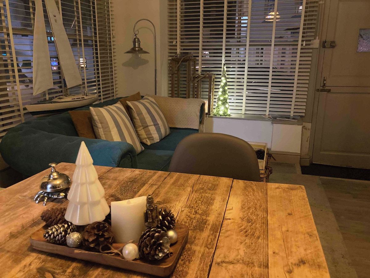 Una sala de estar acogedora con una mesa de madera, un centro decorativo y una maqueta de un velero en el alféizar.