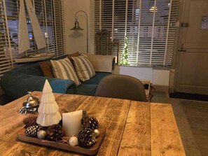 Una sala de estar acogedora con una mesa de madera, un centro decorativo y una maqueta de un velero en el alféizar.