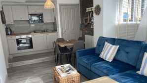 Ein gemütlicher, kleiner Wohnraum mit einer Küchenzeile, einem Essbereich und einem blauen Sofa mit gestreiften Kissen.