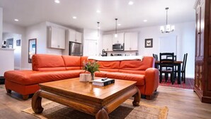A modern living room with a sectional sofa, a wooden coffee table, and a kitchen in the background. - Brand New 3 BR Vacation Home on a Golf Course (Victor)