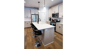 A modern kitchen with white cabinets, a stainless steel refrigerator, a microwave, and a bar area with stools. - Brand New 3 BR Vacation Home on a Golf Course (Victor)