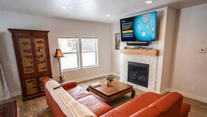 A living room with a red sofa, a wooden coffee table, a fireplace, and a television mounted above it. - Brand New 3 BR Vacation Home on a Golf Course (Victor)