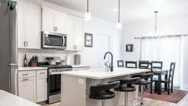 A modern kitchen with white cabinets, stainless steel appliances, and a central island with bar stools. - Brand New 3 BR Vacation Home on a Golf Course (Victor)