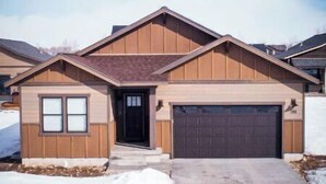 A single-story house with a front garage, a small porch, and a snow-covered driveway. - Brand New 3 BR Vacation Home on a Golf Course (Victor)