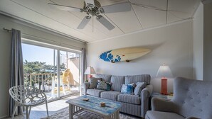 A living room with a grey sofa, a white chair, a coffee table, and a surfboard on the wall. - 1 Bedroom, Sleeps 4, Balcony w/ Ocean View (Ocean City)