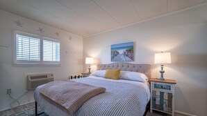 A bedroom with a large bed, two bedside tables with lamps, a window with blinds, and a painting on the wall. - 1 Bedroom, Sleeps 4, Balcony w/ Ocean View (Ocean City)