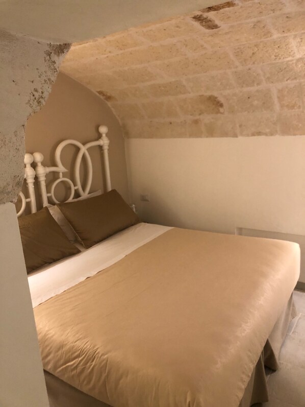Un lit avec une tête de lit, un mur en pierre et un plafond blanc.