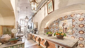 Une cuisine dotée d’un plan de travail en marbre, de luminaires suspendus et d’un mur recouvert de carreaux, orné d’une fresque à thème religieux.