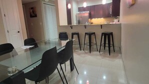 Un'area pranzo moderna con tavolo in vetro, sedie nere e un bancone bar con sgabelli.