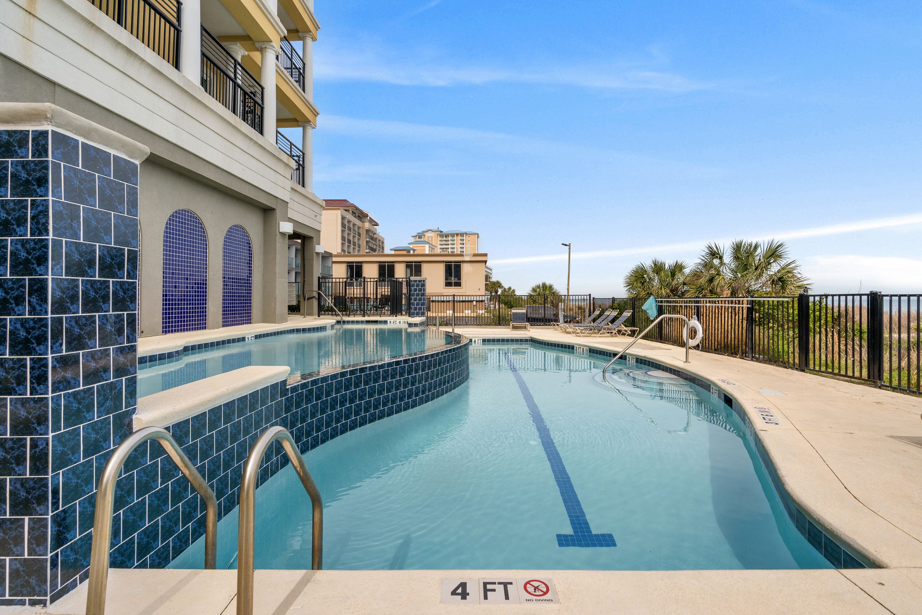 A swimming pool with a 4 FT depth marker, surrounded by a poolside area with lounge chairs and a railing.