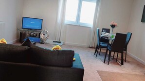 A living room with a sofa, a dining table with chairs, a TV, and a radiator. - Remarkable 2-bed Apartment in Reading (Reading)