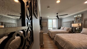 A hotel room with two beds, a ceiling fan, a large window, and a decorative wall panel.