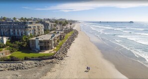 A coastal residential area with a beach, houses, and a pier in the distance.