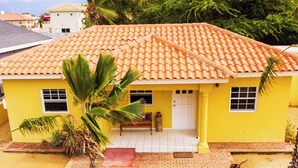 Una casa amarilla con techo de tejas, un porche y una palmera en primer plano.