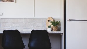 A kitchen with two black chairs, a wooden cutting board, and two potted plants on the counter. - RYDER FLATS UNIT 2 - Close to Beaches (South West Rocks)