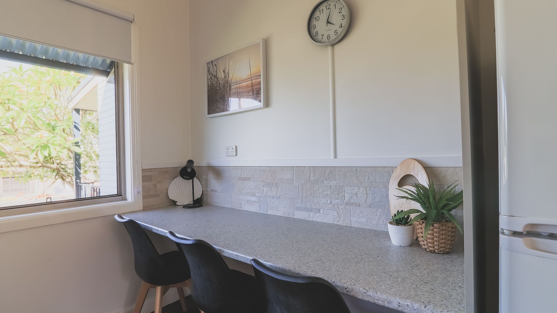 A kitchen with a granite countertop, a clock, a framed picture, and a potted plant.