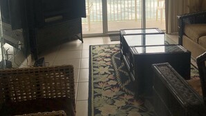 A living room with a television, wicker furniture, a glass coffee table, and a view of the ocean through a sliding glass door. - Beautiful beach condo for rent (Panama City beach)
