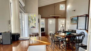 A spacious kitchen with wooden flooring, a dining area with a round table and chairs, and a small seating area with a bench. - Absolute lake front - lie in bed & listen to the fish jump! (Green Point)