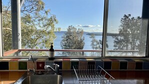 A kitchen with a stainless steel sink, a dish rack, and a window overlooking a lake with trees. - Absolute lake front - lie in bed & listen to the fish jump! (Green Point)