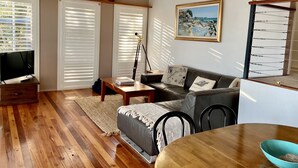 A living room with a wooden floor, a sofa, a coffee table, a TV, and a painting on the wall. - Absolute lake front - lie in bed & listen to the fish jump! (Green Point)