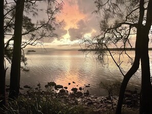 A serene lakeside view with trees framing the scene, calm water, and distant landforms. - Absolute lake front - lie in bed & listen to the fish jump! (Green Point)