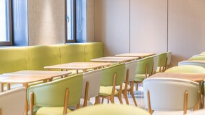 A classroom with rows of tables and chairs, a green cushioned bench, and large windows.