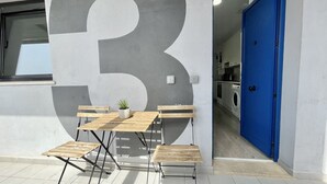 Un espacio moderno al aire libre con mesa y bancos, un número '3' grande en la pared y una puerta azul que da a un cuarto de lavandería.