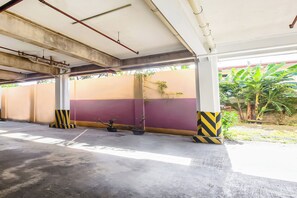 An indoor parking area with concrete pillars, potted plants, and a view of a building with a yellow and pink wall. - Vaccinated Staff - OYO 847 Cote D' Azure (Las Pinas)