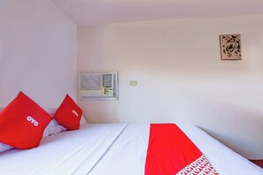 A hotel room with a bed, two red pillows, a wall-mounted air conditioner, and a small wall decoration. - Vaccinated Staff - OYO 847 Cote D' Azure (Las Pinas)