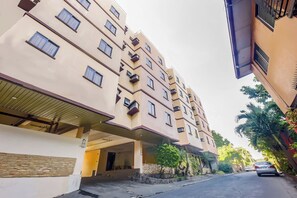 Un edificio residencial de varios pisos con balcones, un acceso cubierto y vista a la calle.