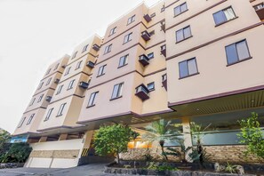A multi-story residential building with balconies, a stone facade, and a landscaped garden area. - Vaccinated Staff - OYO 847 Cote D' Azure (Las Pinas)