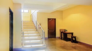A staircase with a metal railing leading to a landing, a wooden door, and a small table with a plant. - Vaccinated Staff - OYO 847 Cote D' Azure (Las Pinas)