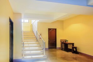 A staircase with a metal railing leading to a landing, a wooden door, and a small table with a plant. - Vaccinated Staff - OYO 847 Cote D' Azure (Las Pinas)