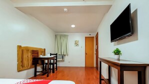 A hotel room with a bed, a desk, a chair, a television, and a small plant. - Vaccinated Staff - OYO 847 Cote D' Azure (Las Pinas)
