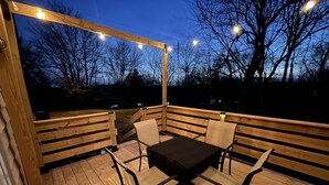 A wooden deck with a table and chairs, string lights, and a view of trees and a body of water at dusk. - Clayton's 1910, Completely Restored Mill House, business-friendly weekday rates (Graham)
