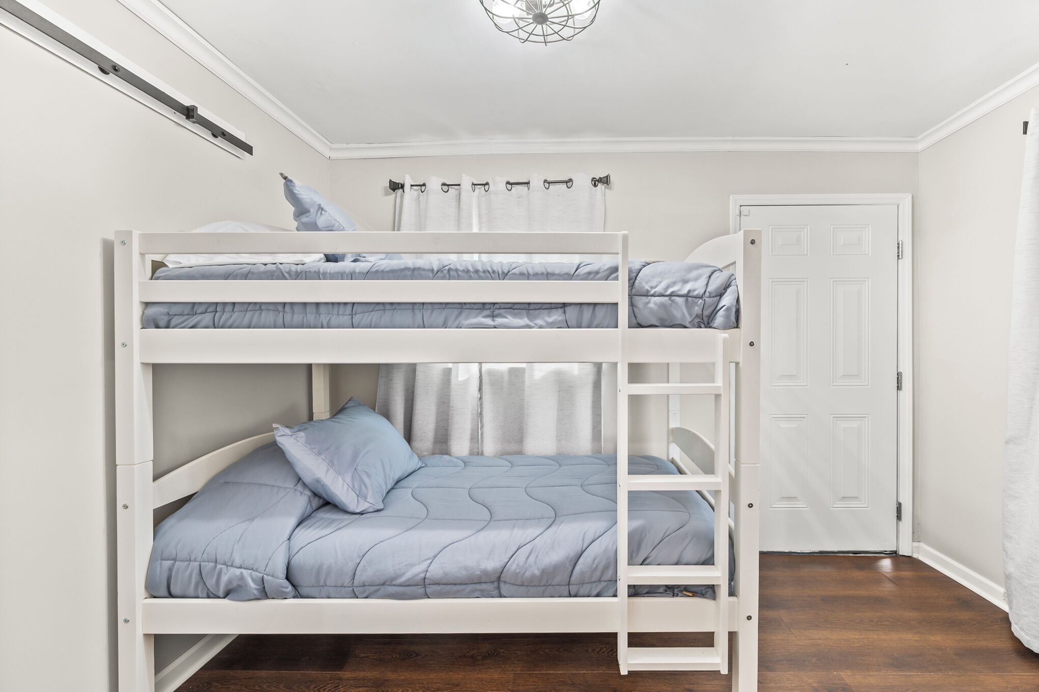 Ein Stockbett mit weißem Gestell und blauer Bettwäsche, eine weiße Tür und ein Holzboden.